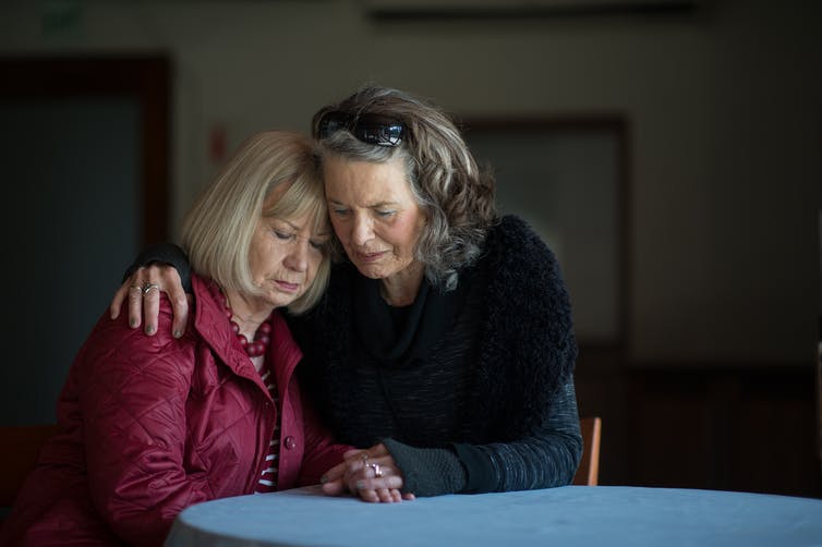 A woman puts her arm around the shoulders of a friend.