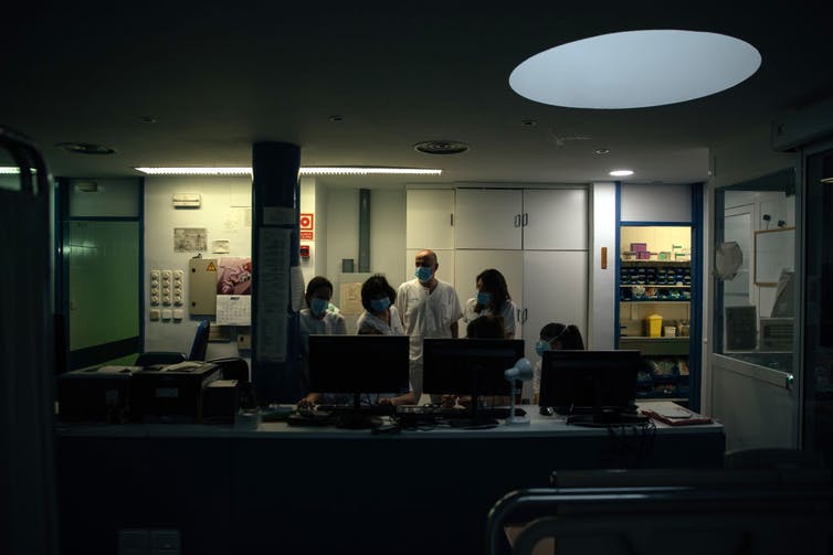 Health care workers huddled at an ICU nursing station at night.
