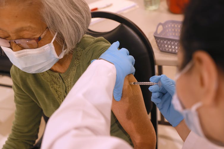 An elderly woman wearing a mask receives a shot.