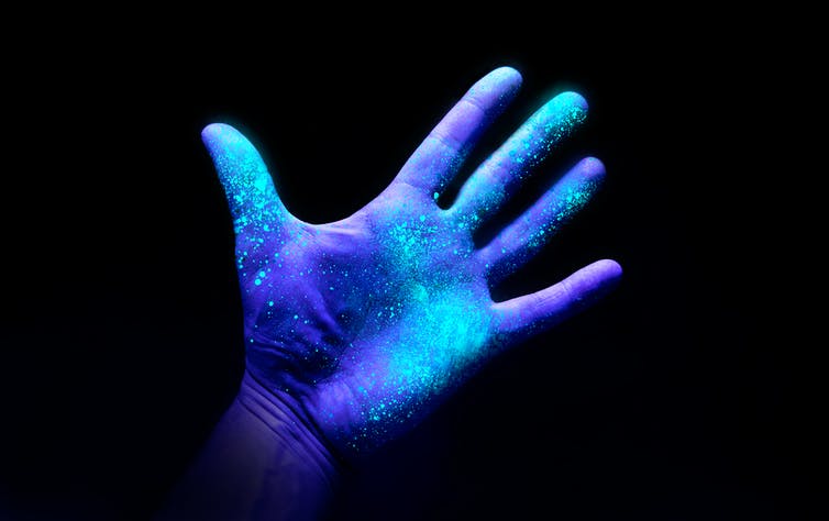 A hand under UV light glowing in many places.