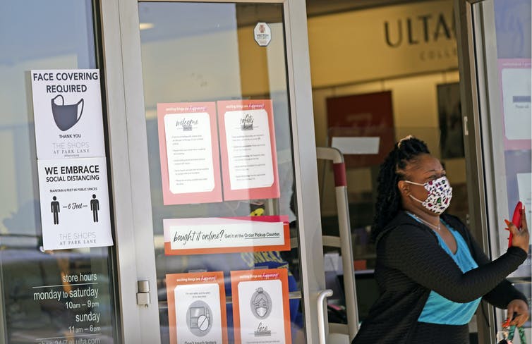 A woman exiting a store with signs showing mask requirements on the door.
