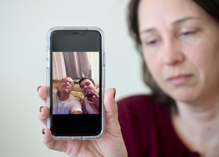 Woman holding up phone with image of brother and son who died after taking fentanyl-laced drugs
