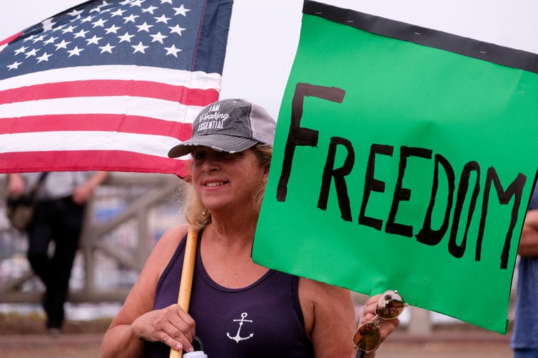 Anti-vaccination protester holds a sign and a flag during a rally against COVID-19 vaccines