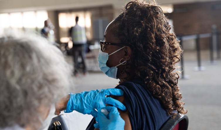 A woman wearing a mask gets a COVID-19 vaccine