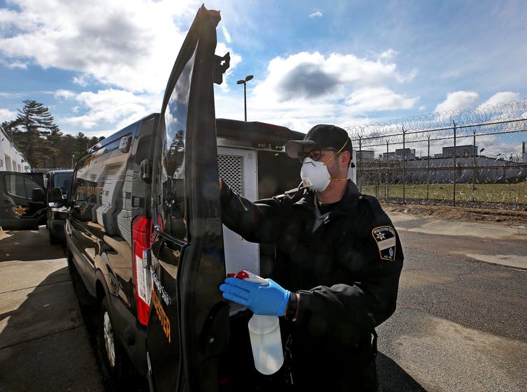 Wearing a protective mask and gloves, a correctional officer sanitizes an inmate transport van.