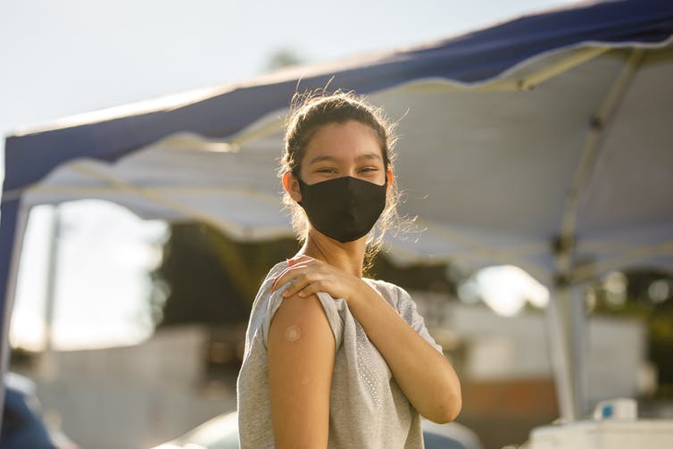 Teen girl wearing a mask and showing a bandaid on her forearm