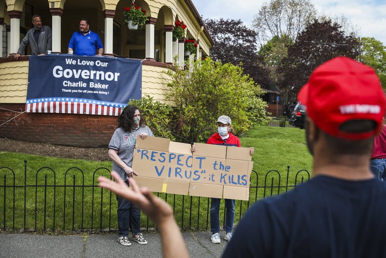 two masked people hold homemade sign that reads 'Respect the virus, it kills'