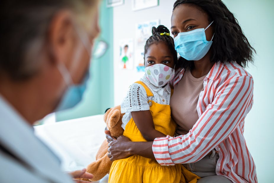Woman wearing a face mask holding her child talking to a health care provider.