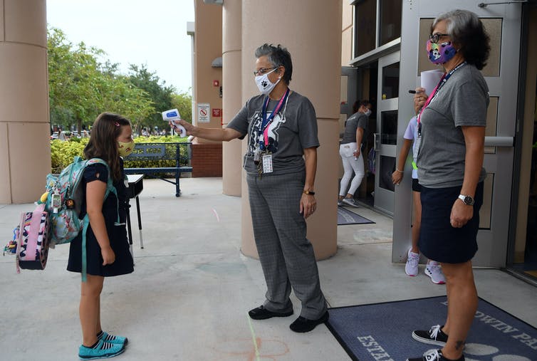 Masked student receives temperature check on way in to school