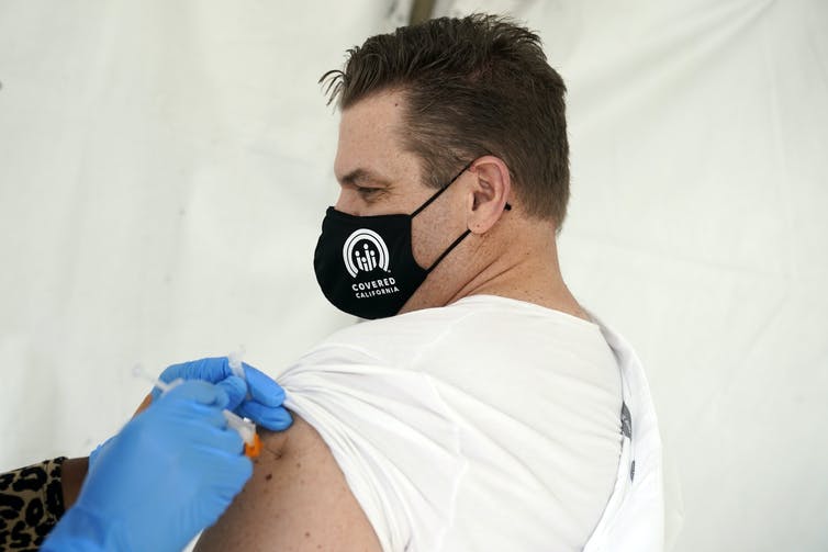 A man wearing a mask getting his COVID-19 vaccine shot.