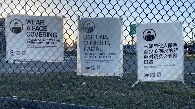 coronavirus precaution signs in multiple languages hang on a fence