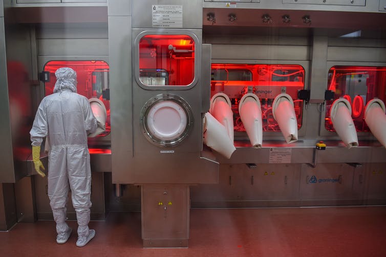 An employee in full protective gear works on assembling vaccine doses.