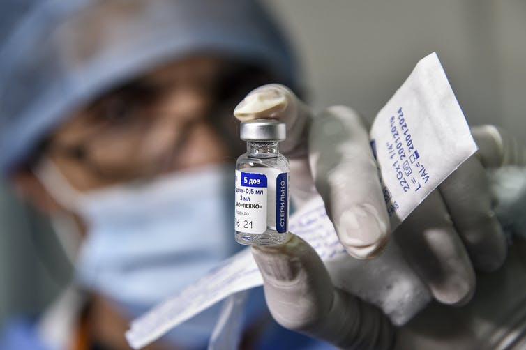 A person wearing a mask and gloves holds up a small vial.