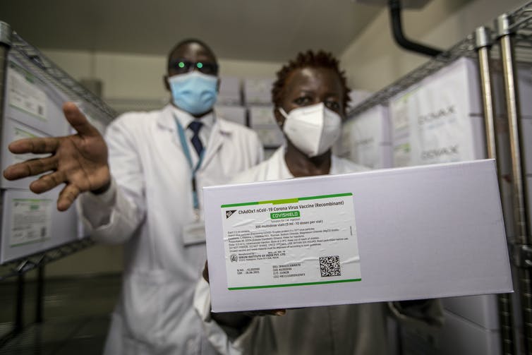 Two people in lab coats hold a box showing the label