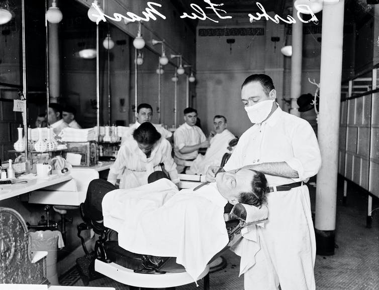 masked barber shaves a customer