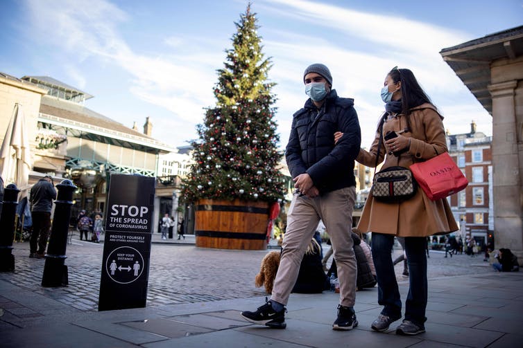 masked people walk past a public Christmas tree