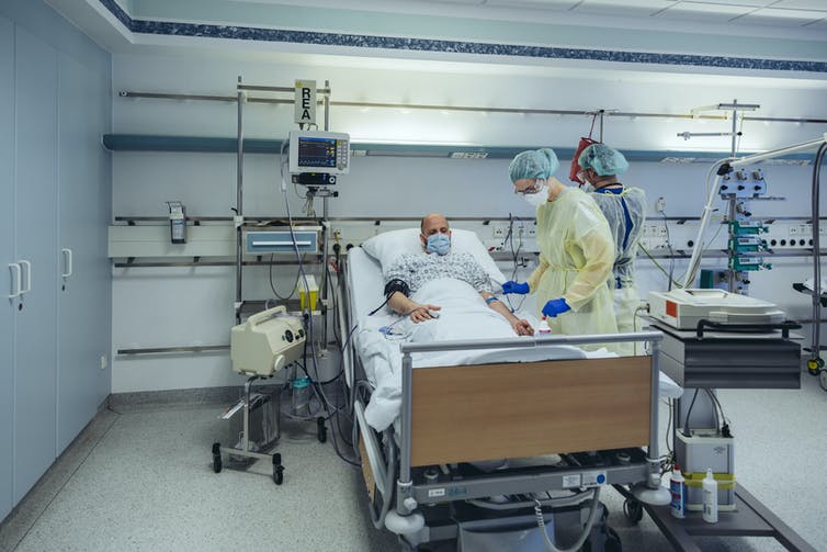 A doctor treating a patient in a hospital bed, both wearing masks.