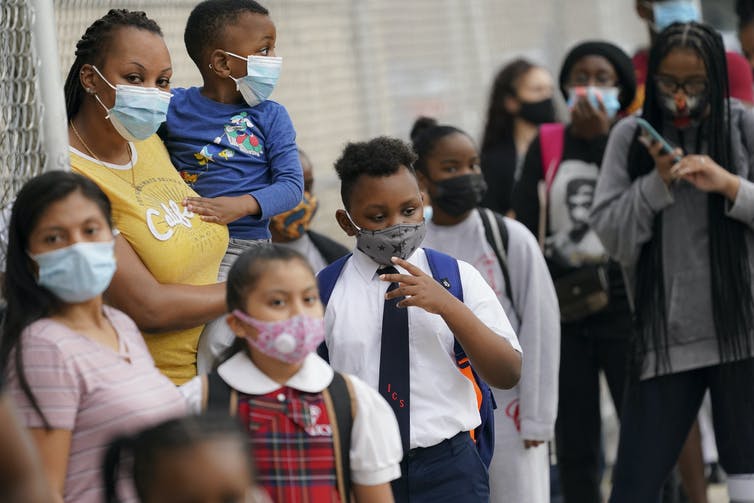 Children and parents wait outside a New York City school wearing masks.