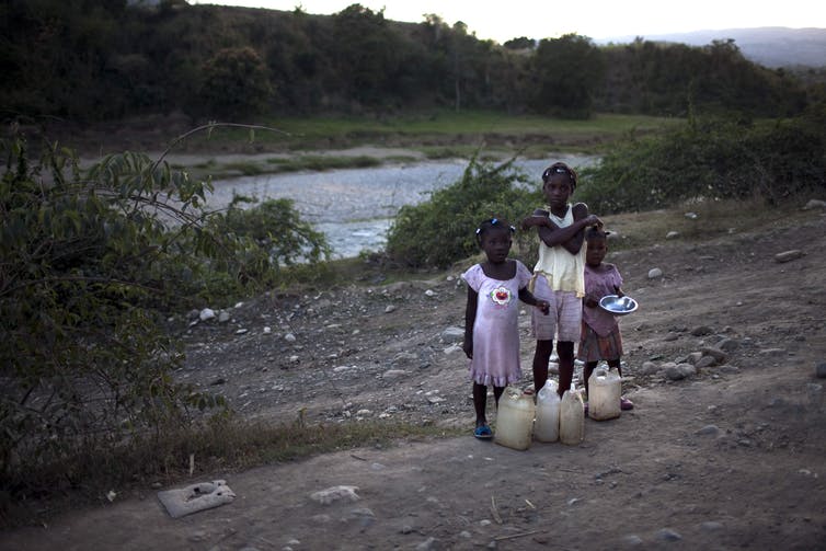 Three young girls stand on the side of a dirt rod in Haiti.