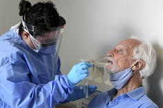 A medical professional inserting a nasal swab into an older man's nose.