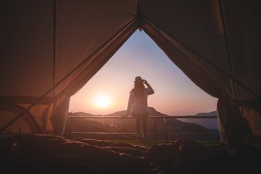 Woman traveler sitting outside camping tent and looking at sunrise view and mountain range.Travel outdoors camping for exploration and freedom concept.
