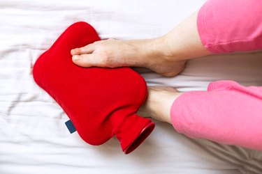 Person with cold feet in bed with a red hot-water bottle