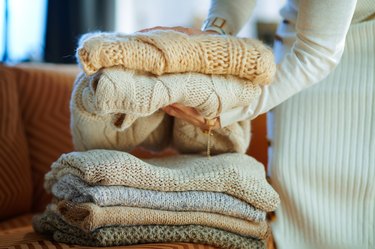 Closeup on woman near couch folding sweaters for storage