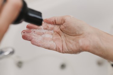 Cropped Hands Of Woman Removing Shampoo From Bottle In Bathroom