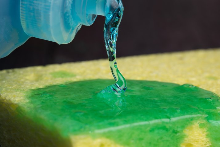 Close-Up Of Dishwashing Liquid Being Spread On Cleaning Sponge