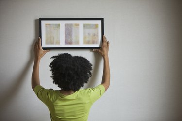 Mixed race woman hanging picture on wall