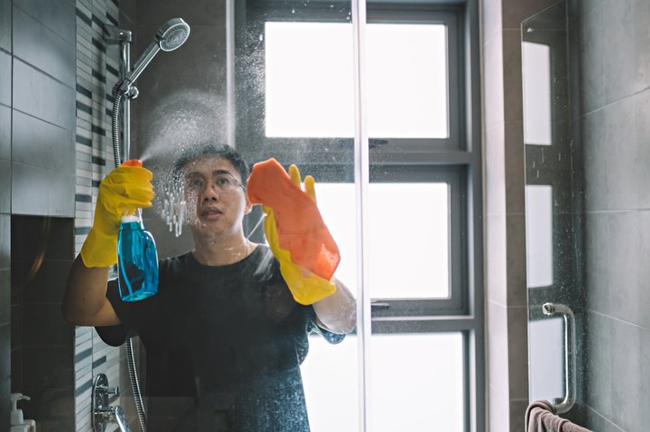 asian chinese male cleaning home with yellow gloves and orange colored cloth