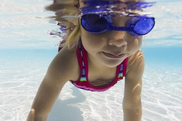 underwater lifestyle shot of a female toddler in goggles as she learns to swim in a pool