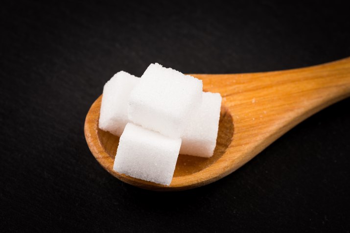 White refined sugar in wooden spoon on dark stone background