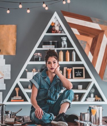 Woman in coveralls sits on table in front of wooden shelf