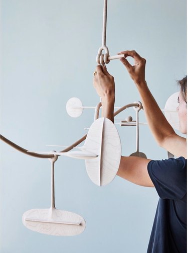 A woman's hands and arms adjust a hanging wooden sculpture