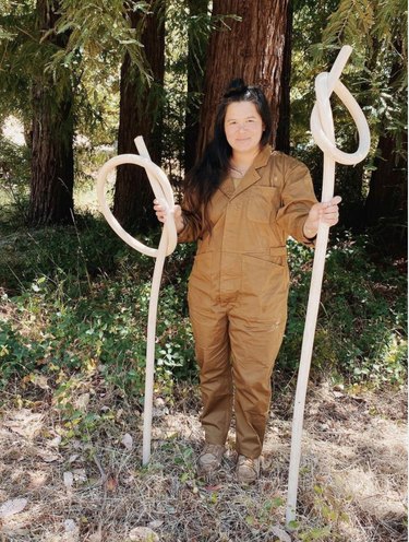 Woman stands in front of trees holding wooden knot sculptures