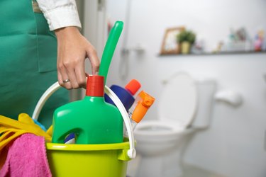 The cleaning woman is standing in the bathroom holding a blue bucket full of chemicals and facilities for storing her hands.