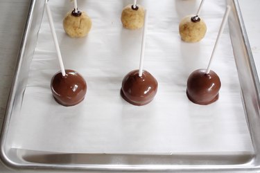 Three cake pops coated in chocolate candy and placed onto parchment-lined tray