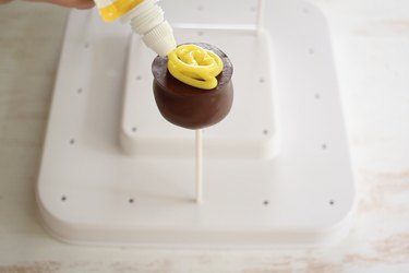 Piping yellow icing onto center of cooled cake pop