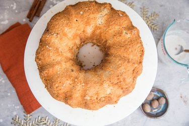 naked bundt cake on a cake stand and measuring cup of glaze