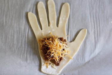 Meat and cheese filling on top of dough shaped like hand
