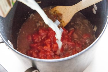 pouring chicken broth into pot of soup