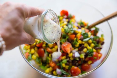 Pouring poppy seed dressing into salad bowl