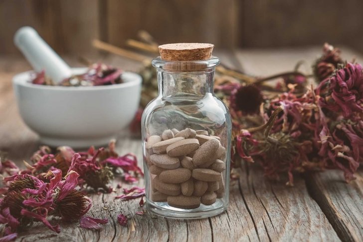 Bottle of herbal pills, mortar of healthy echinacea herbs and dry coneflower bunch on wooden table.