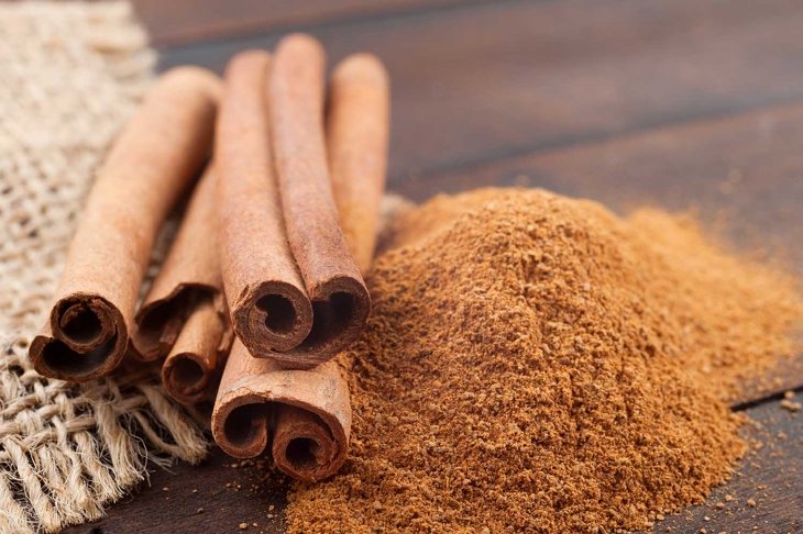 Cinnamon sticks and cinnamon powder on brown wooden board.