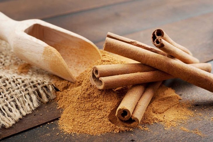 Cinnamon sticks and cinnamon powder in wooden scoop, on table