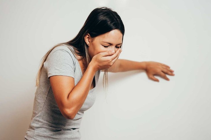 Portrait of young woman drunk or sick vomiting over gray background