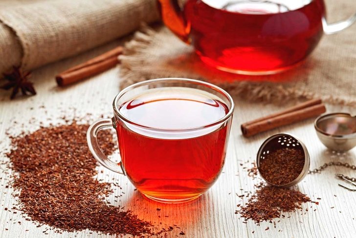 Cup of healthy traditional herbal rooibos red beverage tea with spices on vintage wooden table