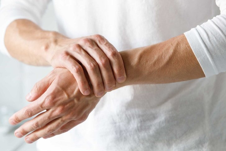 Closeup of male arms holding his painful wrist caused by prolonged work on the computer, laptop. Carpal tunnel syndrome, arthritis, neurological disease concept. Numbness of the hand