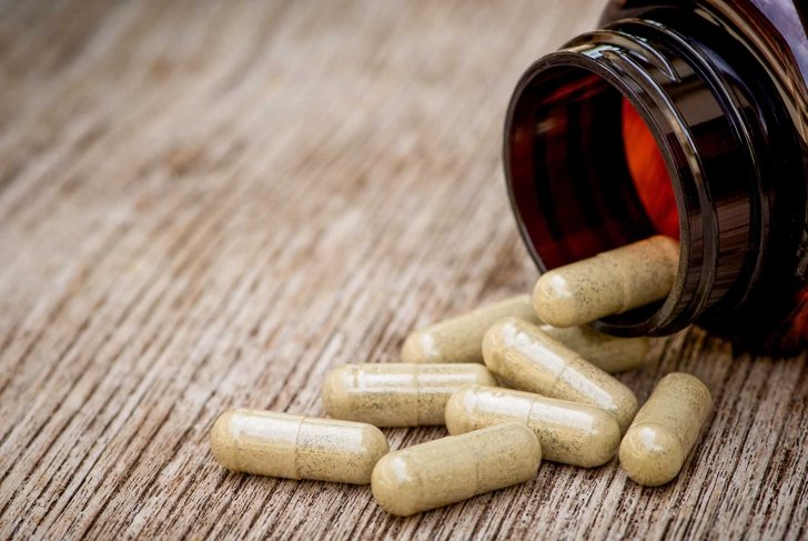 Green natural herbal medicine capsule in brown bottle isolated on old wood table background. Alternative supplement concept.